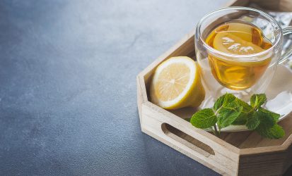 Medicines and Health Healthcare Concept. Cup of hot tea with lemons, pills and thermometer on wooden tray on concrete table background